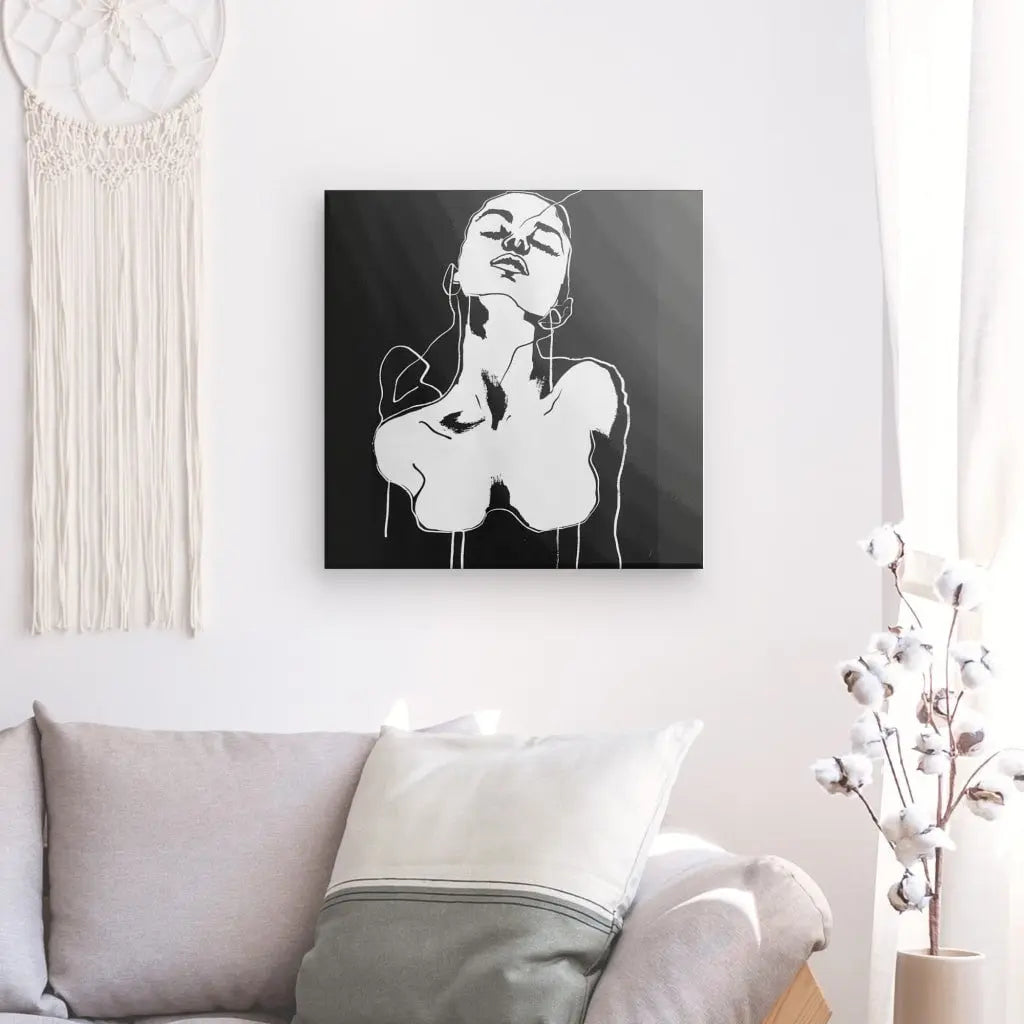 Un Tableau Dessin Femme Noir et Blanc Art Moderne minimaliste est affiché sur le mur au-dessus d'un canapé blanc avec des coussins gris. Une tenture murale en macramé est à gauche, et un rideau blanc et une plante à droite, créant une décoration intérieure élégante.