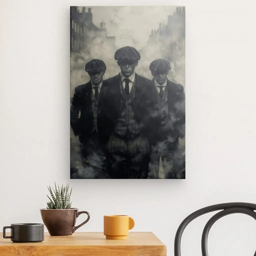 Un Tableau Peinture Gang Peaky Blinders Monochrome, représentant trois hommes en costumes et casquettes plates marchant vers le spectateur, est accroché sur un mur blanc au-dessus d'une table en bois avec une petite plante et trois tasses à café. Cette décoration intérieure ajoute une touche d'élégance vintage à l'espace.