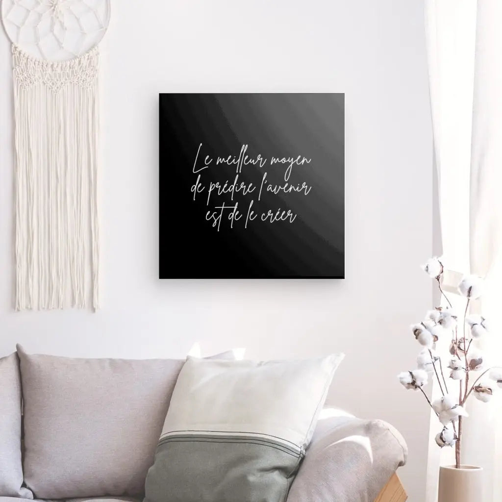 Un mur avec une tenture décorative et un Tableau Citation "Créer son avenir" Noir et Blanc Minimaliste avec une œuvre d'art encadrée indiquant "Le meilleur moyen de prédire l'avenir est de le créer" au-dessus d'un canapé avec des coussins, illustrant une décoration intérieure sophistiquée. .