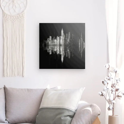 Un salon comprend un canapé gris clair avec un coussin blanc et gris, une œuvre d'art paysage urbain abstrait en noir et blanc sur le mur et un mur en macramé beige suspendu à côté du Tableau Ville Building Dessin Moderne Monochrome. Ce décor intérieur combine une esthétique moderne avec des éléments chaleureux pour une atmosphère invitante.