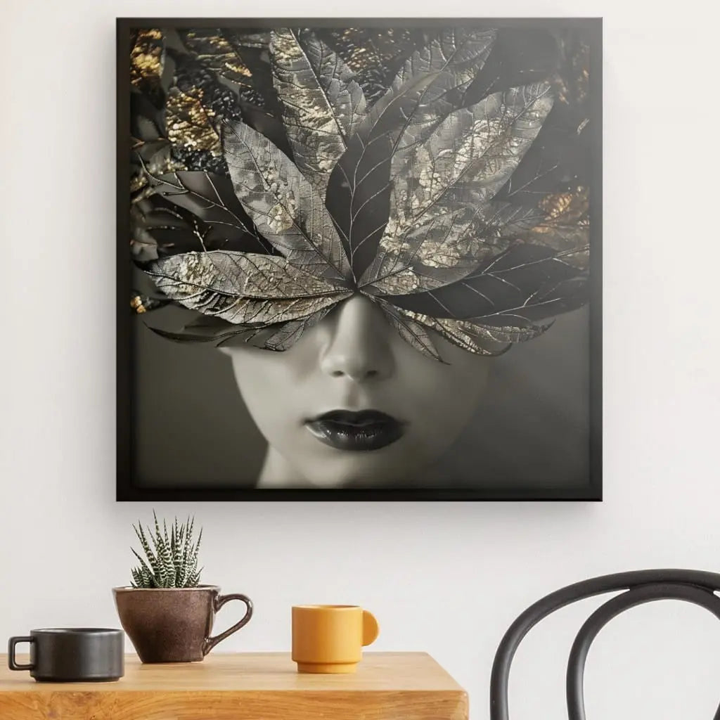 Le Tableau Visage Femme Plumes Dorées Noir et Blanc est accroché au mur au-dessus d'une table en bois avec deux mugs, une petite plante et une chaise noire - parfait pour toute décoration contemporaine.