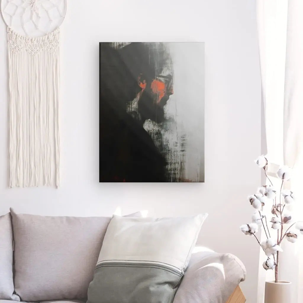 Un salon minimaliste comprend un canapé gris avec un oreiller blanc et gris, un tableau mural Portrait Homme Peinture Noir Blanc Orange, une tenture murale en macramé et un cotonnier dans un vase, le tout contribuant à une décoration globale moderne.