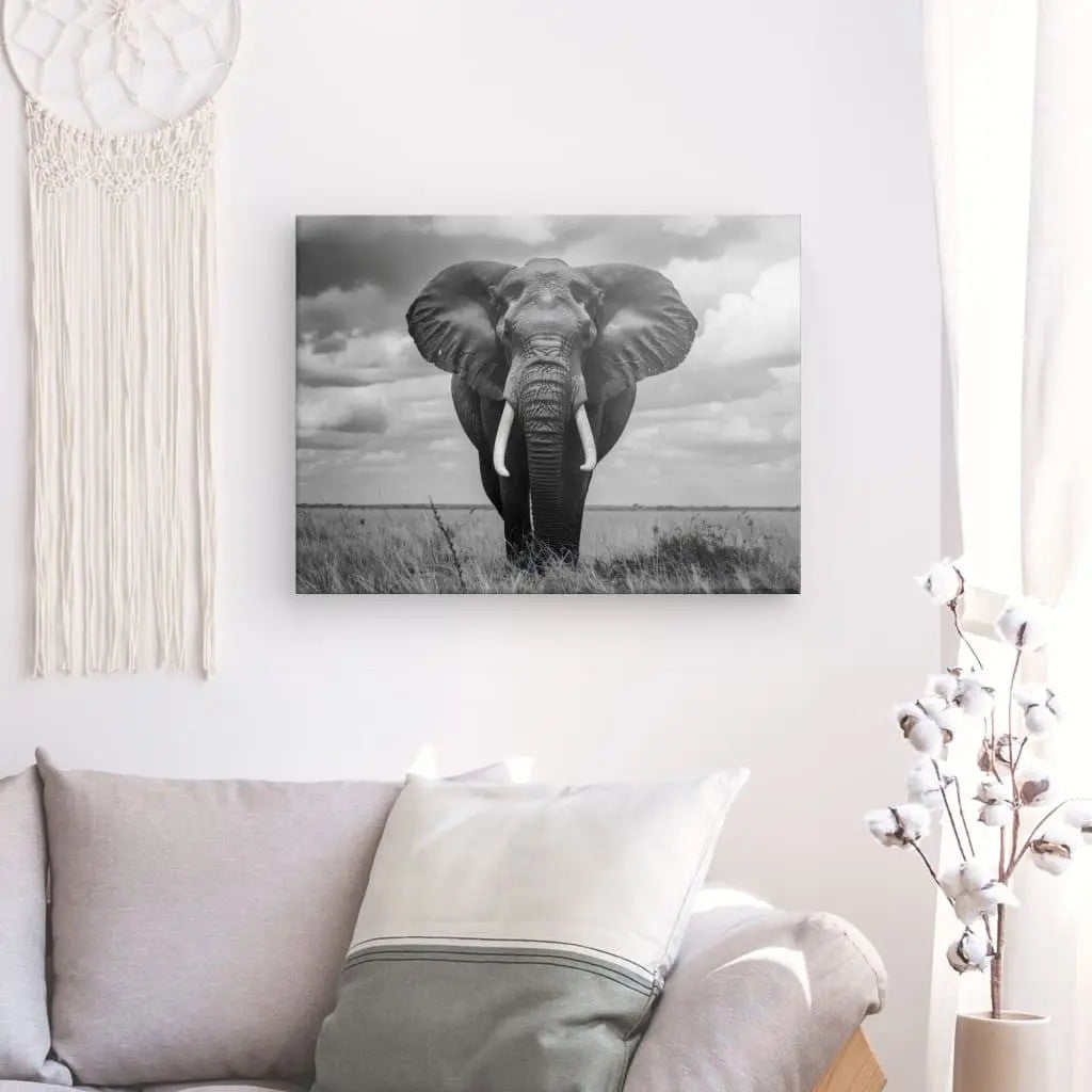 Une photographie monochrome, le Tableau Éléphant d'Afrique Noir et Blanc, est accrochée sur un mur blanc au-dessus d'un canapé beige orné de coussins gris. La décoration intérieure sophistiquée est complétée par une tenture murale et une plante en pot.