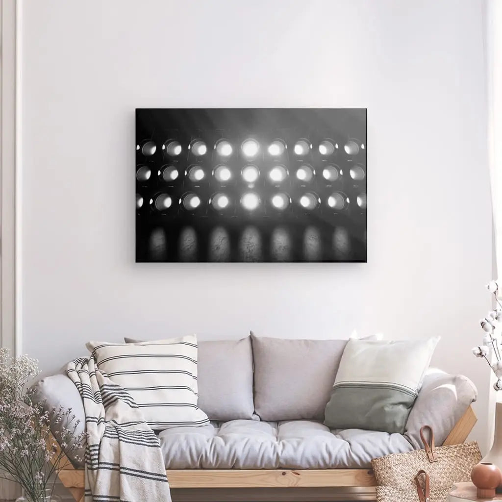 Un canapé gris avec des oreillers assortis et une couverture dans une pièce minimaliste, mettant en vedette les Tableau Projecteurs Lumineux Noir et Blanc avec des lumières circulaires sur le mur au-dessus.