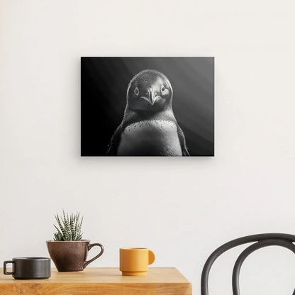 Le Tableau Manchot Portrait Animalier Noir et Blanc, élégamment encadré et accroché sur un mur blanc, complète la table en bois ornée d'une plante en pot et de deux tasses, ajoutant une touche de décoration d'intérieur sophistiquée.