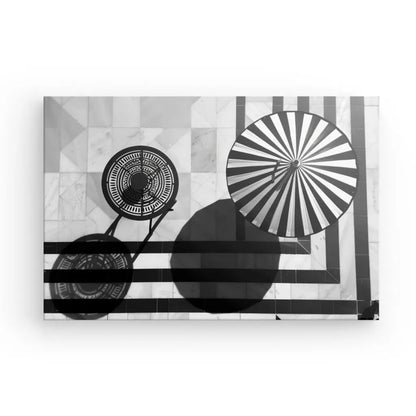 Image du Tableau Bord de Piscine Été Noir et Blanc, présentant une table circulaire à motifs et un parasol projetant des ombres sur une surface carrelée, créant une ambiance relaxante qui respire une décoration chic.