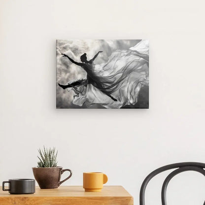 Un Tableau Chorégrapie Aérienne Femme Drapée monochrome est accroché sur un mur blanc au-dessus d'une petite table avec une plante en pot, une tasse marron et une tasse jaune. Une chaise noire est partiellement visible, ajoutant à la décoration intérieure chic.