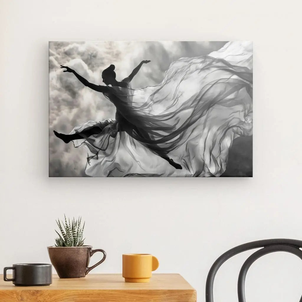 Le Tableau Chorégraphie Aérienne Femme Drapée Monochrome, une photographie encadrée en noir et blanc d'une danseuse en plein saut et une superbe œuvre d'art contemporain, est accrochée sur un mur blanc au-dessus d'une table avec une plante en pot et deux tasses, créant un élégant tableau monochrome. dans votre décoration intérieure.