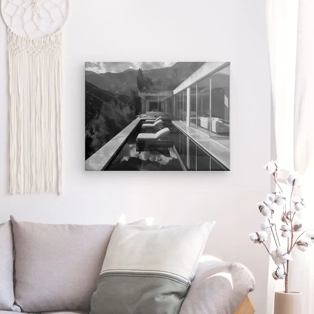 Une photographie en noir et blanc d'une maison moderne avec piscine, intitulée "Tableau Villa Architecture Moderne Noir et Blanc", est accrochée sur un mur blanc au-dessus d'un canapé beige orné de coussins. Des objets décoratifs tels qu'un attrape-rêves et une plante rehaussent la décoration intérieure élégante. Cet élégant Tableau Villa Architecture Moderne Noir et Blanc ajoute de la sophistication à la pièce.