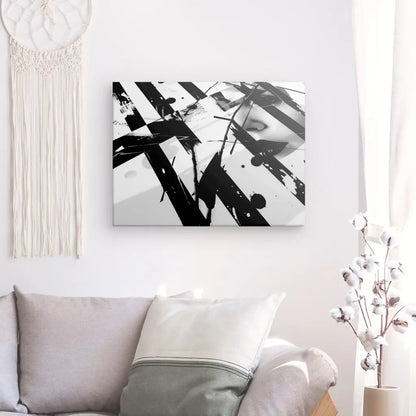 Le Tableau Moderne Patchwork Peinture Visage Noir et Blanc, une œuvre d'art abstraite saisissante, est accrochée sur un mur blanc à côté d'un canapé et d'une tenture murale décorative. Un coussin blanc avec une bordure grise repose sur le canapé, rehaussant l'intérieur artistique.