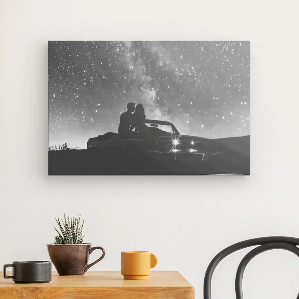 Un Tableau Couple Nuit étoilée Voiture Noir et Blanc est affiché sur le mur, représentant une image en noir et blanc d'un couple dans une voiture vintage sous un ciel étoilé. En dessous, la décoration intérieure comprend une table en bois avec des tasses, une plante en pot et une partie de chaise.