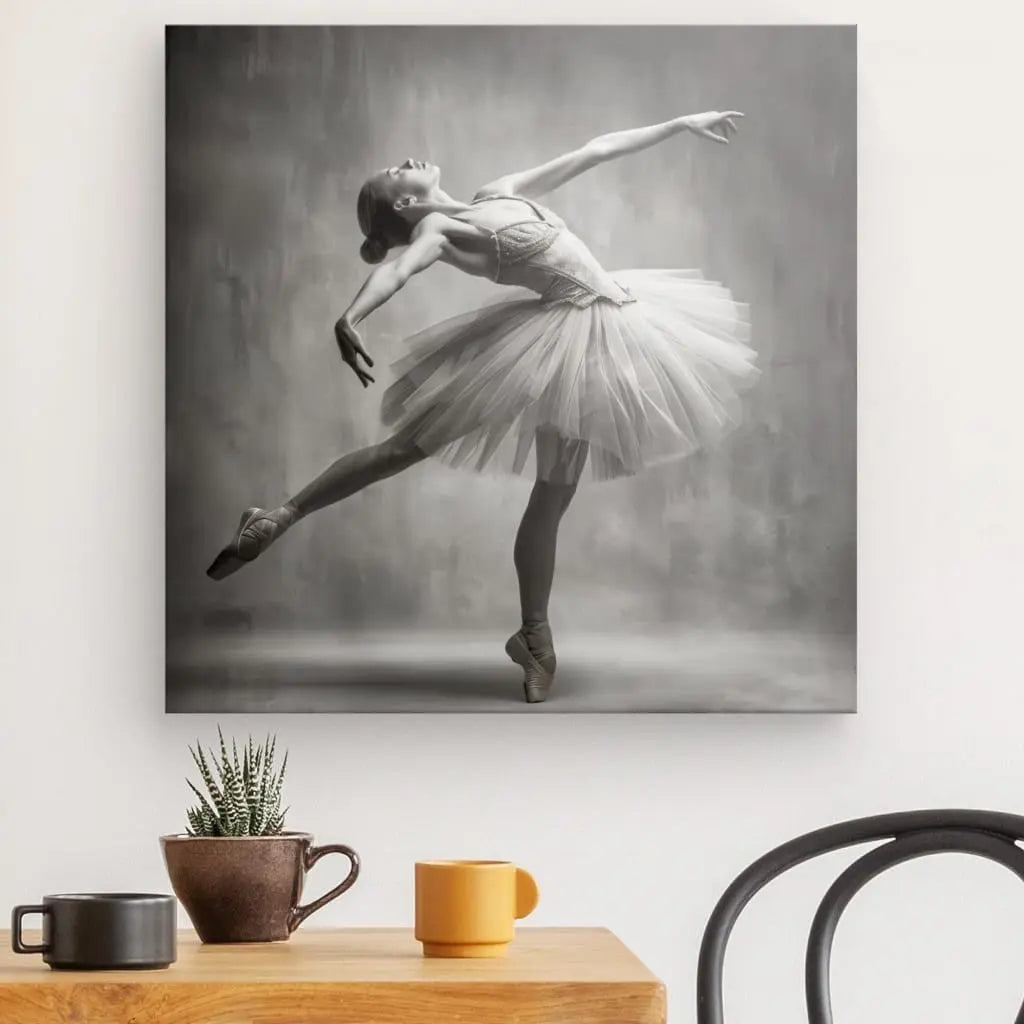 Une photographie monochrome vintage de la collection Tableau Danseuse Étoilée, représentant une danseuse de ballet dans une pose élégante, est encadrée et exposée au-dessus d'une table en bois minimaliste ornée d'une petite plante en pot et de deux tasses. Cette œuvre d'art ajoute une touche de grâce intemporelle à la pièce.