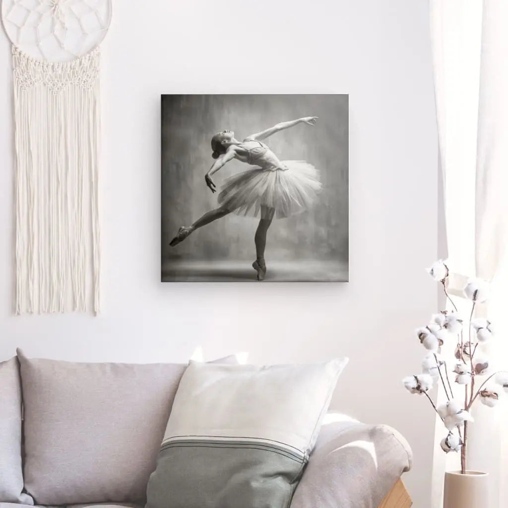 Une photo d'une danseuse de ballet dans une pose rappelant le Tableau Danseuse Etoilée Vintage Monochrome est accrochée au mur au-dessus d'un canapé aux coussins blancs et gris. Une tenture murale en macramé se trouve à gauche et un cotonnier à droite, créant une ambiance rétro d'art monochrome vintage.