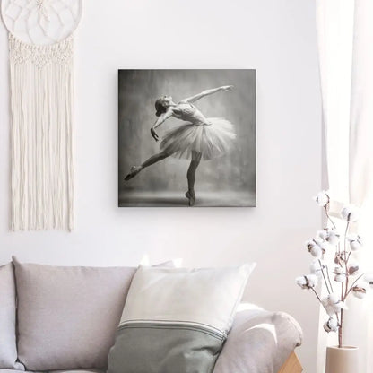 Une photo d'une danseuse de ballet dans une pose rappelant le Tableau Danseuse Etoilée Vintage Monochrome est accrochée au mur au-dessus d'un canapé aux coussins blancs et gris. Une tenture murale en macramé se trouve à gauche et un cotonnier à droite, créant une ambiance rétro d'art monochrome vintage.