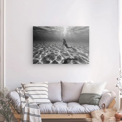 Un salon cosy avec un canapé gris clair, décoré de coussins rayés et unis. Au-dessus du canapé se trouve un saisissant Tableau Plongeuse Fond Sous Marin Noir et Blanc, représentant un nageur sous l'eau.