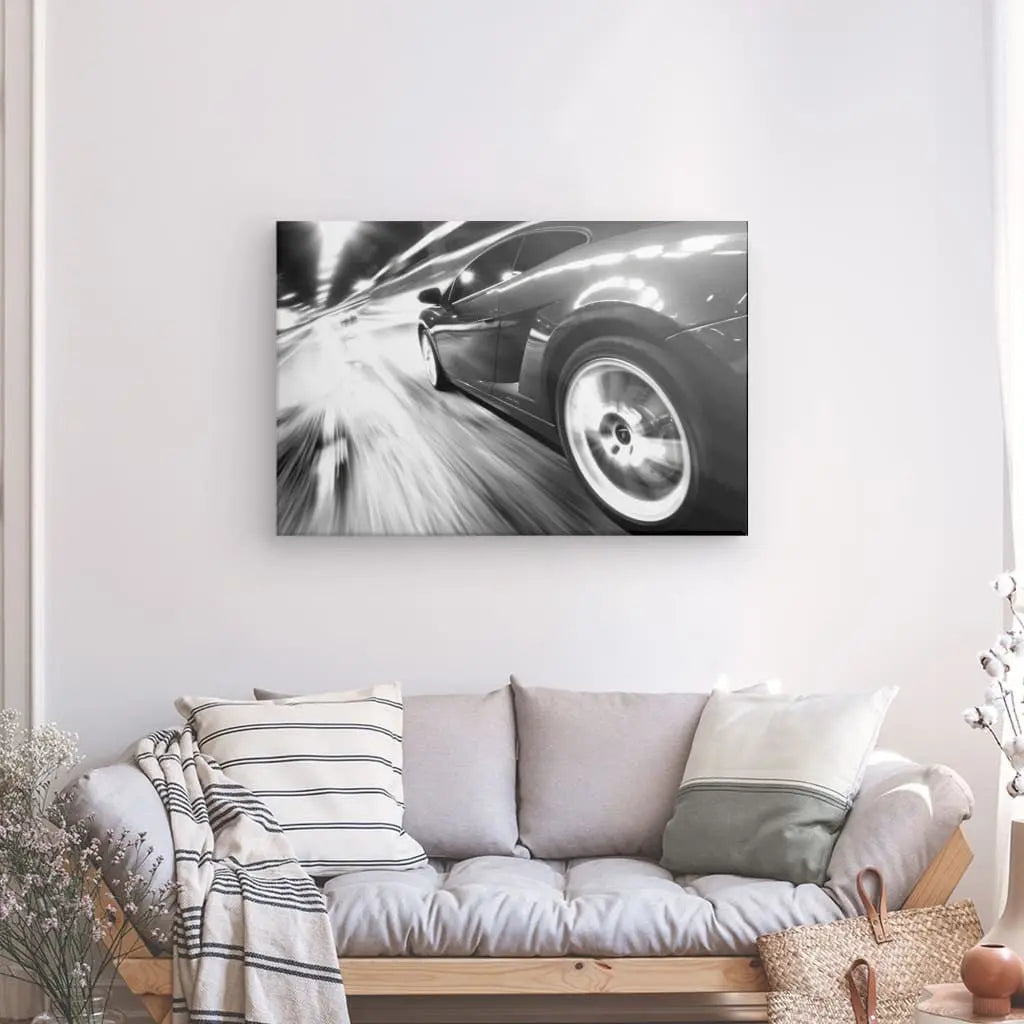 Un Tableau Voiture Autoroute Vitesse Noir et Blanc est exposé au-dessus d'un canapé gris avec des coussins rayés dans un salon moderne, créant une atmosphère de liberté.