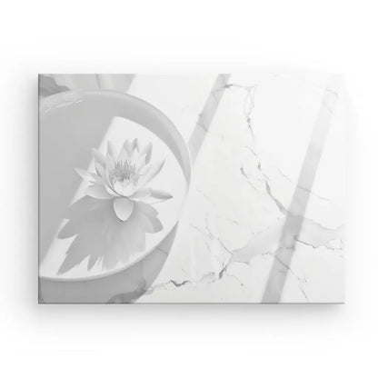 Le Tableau Zen Lotus Blanc et Gris, une image en niveaux de gris d'un seul nénuphar dans un bol rond sur une surface en marbre avec des ombres projetées par des vitres, crée la décoration zen parfaite pour votre espace.