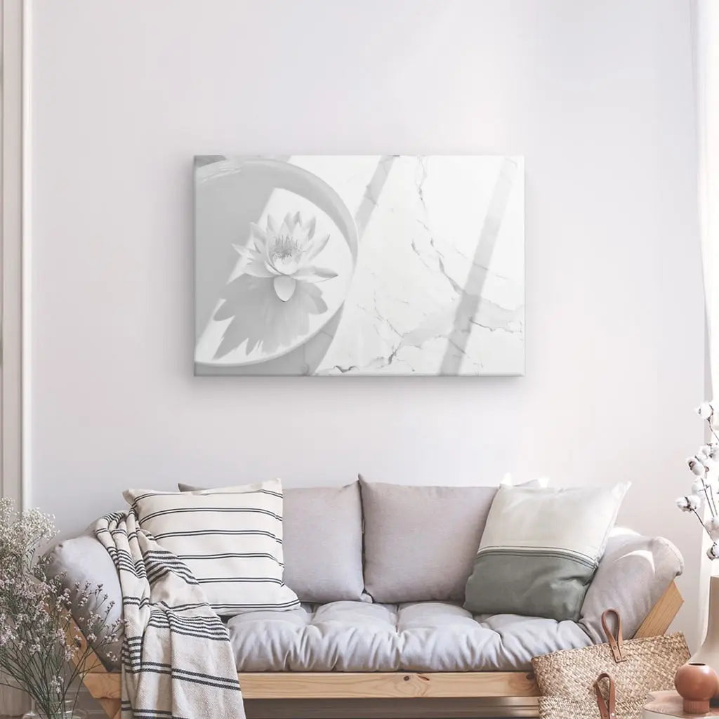 Un salon minimaliste comprend un canapé gris avec des coussins gris et blancs, un coussin à motifs floraux et rayés, un panier tressé et le Tableau Zen Lotus Blanc et Gris dans un plat circulaire.