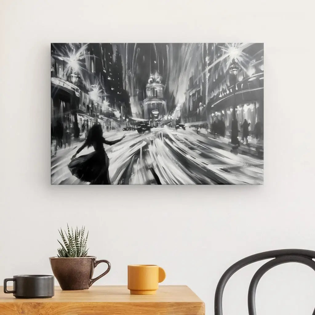 Le Tableau Peinture Scène Danse Rue Parisienne Monochrome, monté sur un mur blanc au-dessus d'une table en bois ornée d'une plante, d'une tasse et d'un mug jaune, à côté d'une chaise noire, représente une scène de rue animée avec des traînées lumineuses à Paris. Cette œuvre captivante dégage un air de romantisme.