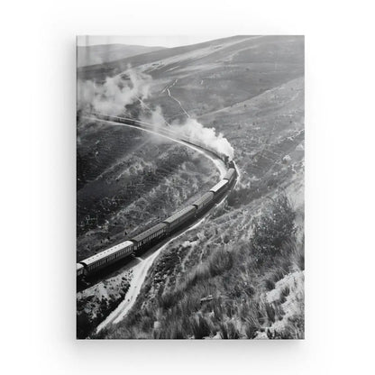 Un train à vapeur traverse un paysage vallonné, émettant de la fumée blanche, avec plusieurs wagons naviguant sur les voies sinueuses à travers le terrain. La zone est herbeuse et peu végétalisée, ressemblant à la reproduction photographique aux couleurs saturées sur toile à texture fine du Tableau Collines Far West Train Vapeur Noir et Blanc.