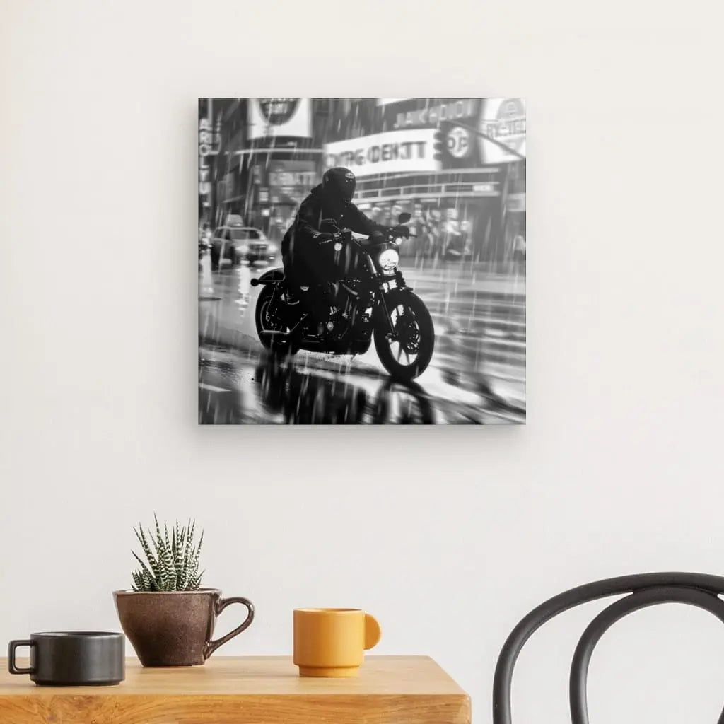 Une photo en noir et blanc d'un motocycliste roulant sous la pluie, intitulée « Tableau Motard Ville Pluvieuse Nuit Noir et Blanc », imprimée avec des encres HP latex sur une toile à texture fine, est montée sur un mur blanc au-dessus d'une table en bois avec une tasse orange, une tasse marron et une petite plante en pot.