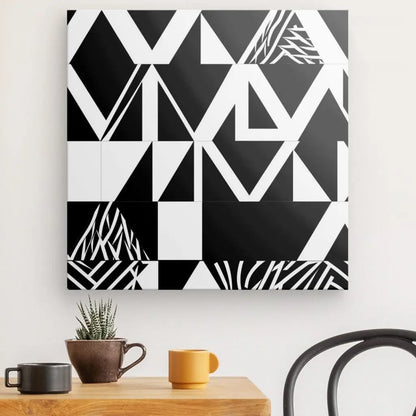 Chef-d'œuvre géométrique, le « Tableau Formes Noires Abstraites Fond Blanc », incarnant le chic minimaliste, est accroché au mur au-dessus d'une table en bois ornée d'une petite plante en pot, d'un mug marron et d'un mug jaune. Une chaise en métal noir est partiellement visible à droite.