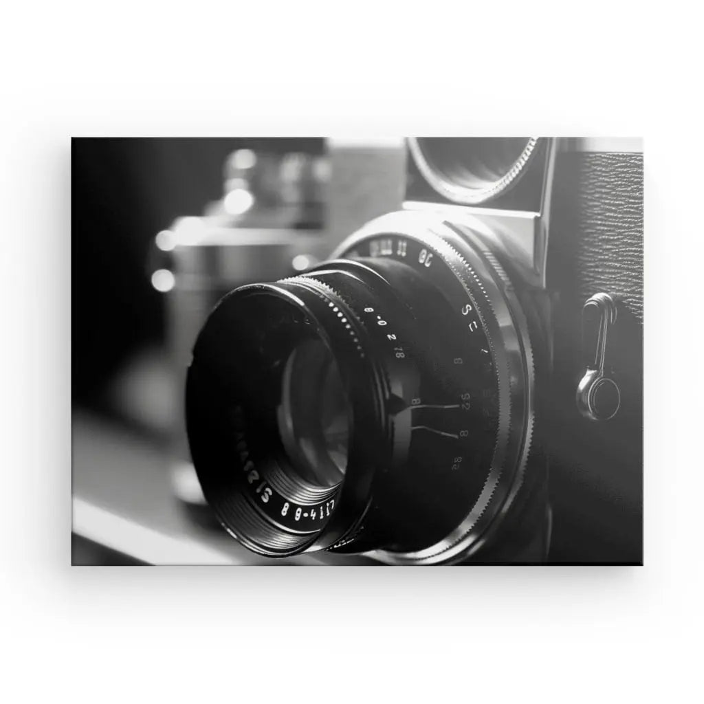 Image en gros plan noir et blanc d'un appareil photo vintage faisant la mise au point sur l'objectif, avec un autre appareil photo vintage flou en arrière-plan. Ce superbe Tableau Photo Objectif Obturateur Noir et Blanc est parfait pour ajouter une touche de photographie classique à votre décoration intérieure.