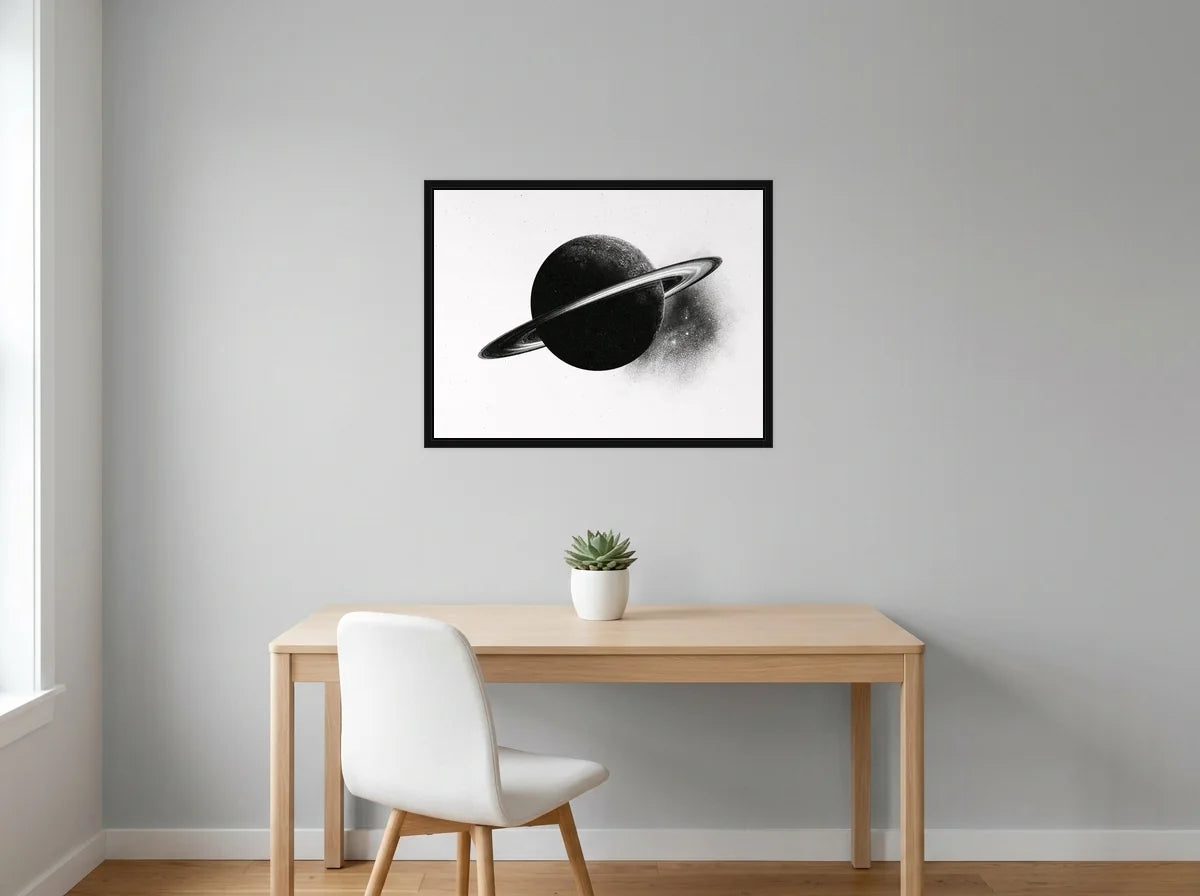 Tableau saturne aux anneaux lumineux noir et blanc en toile encadrée noire, présenté dans : bureau gris clair lumineux