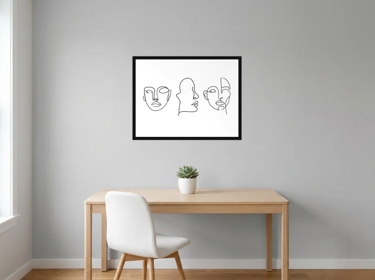Tableau Trois Visages au Trait noir et blanc en toile encadrée noire, présenté dans un bureau gris clair lumineux