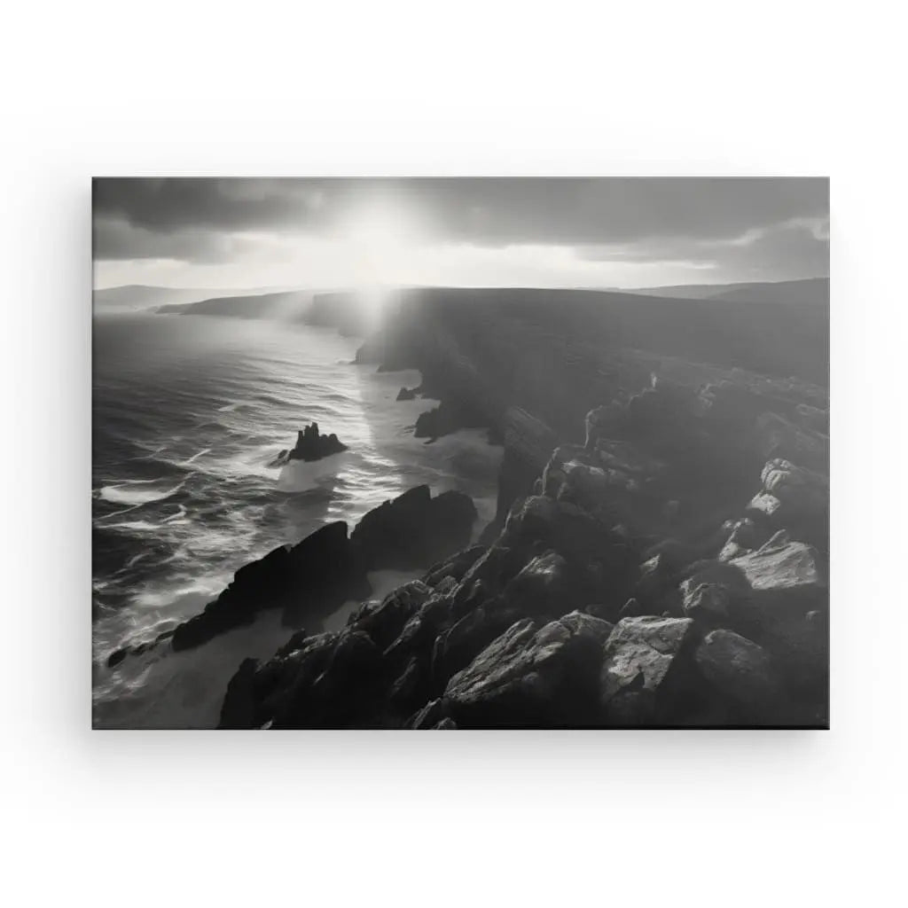 Photo en noir et blanc d'une côte rocheuse en Bretagne, avec le soleil qui brille à travers les nuages, éclairant l'océan et les falaises déchiquetées ; un véritable Tableau Paysage Maritime Bretagne Falaises Noir et Blanc.