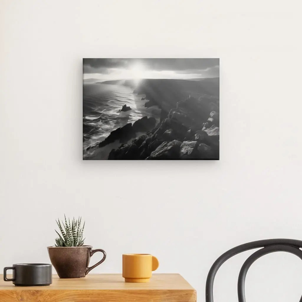 Photographie de paysage encadrée en noir et blanc d'un Tableau Paysage Maritime Bretagne Falaises Noir et Blanc avec des rochers, accroché sur un mur blanc au-dessus d'une table en bois avec une petite plante et une tasse.