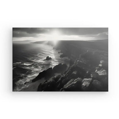 Photographie en noir et blanc d'un paysage côtier spectaculaire en Bretagne, mettant en valeur des falaises rocheuses et des vagues océaniques agitées sous un ciel nuageux percé par la lumière du soleil. Ce saisissant Tableau Paysage Maritime Bretagne Falaises Noir et Blanc capture la beauté brute du paysage maritime.