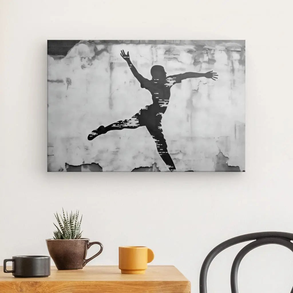 Art mural en noir et blanc représentant une personne dans une pose en l’air avec les bras écartés, rappelant les mouvements de basket-ball de rue. Le Tableau Basketteur Underground Tag Noir et Blanc est monté sur un mur de couleur claire au-dessus d'une table en bois avec une plante et deux mugs.