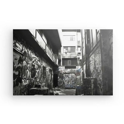 Photographie en noir et blanc d’une ruelle avec des bâtiments des deux côtés, largement couverte de graffitis. Le sol est jonché de débris divers, transformant l'espace en Tableau Underground Urbain Tag Graffitis Noir et Blanc.