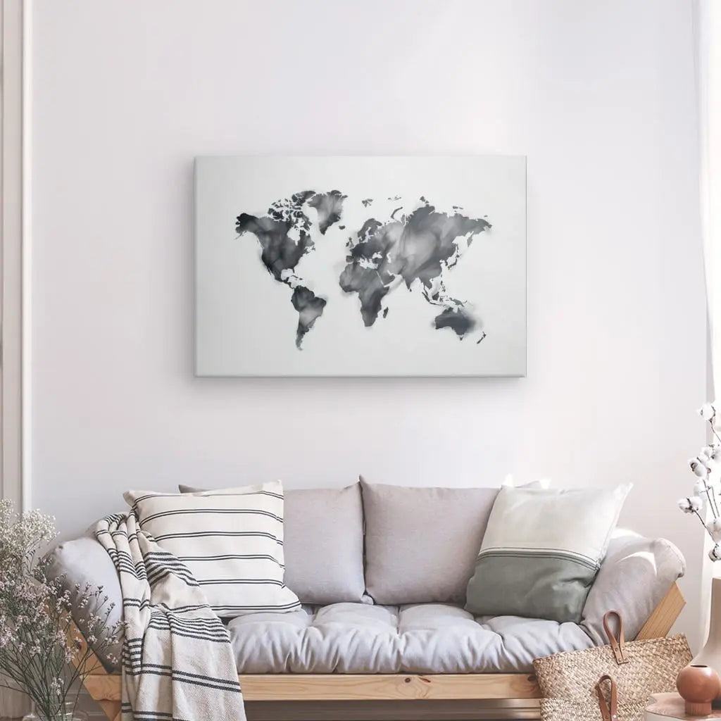 Un canapé gris clair avec des coussins assortis est posé contre un mur blanc avec au-dessus un Tableau Carte du Monde Mapmonde Fumée Noir et Blanc. Un panier et une plante en pot sont positionnés à proximité.