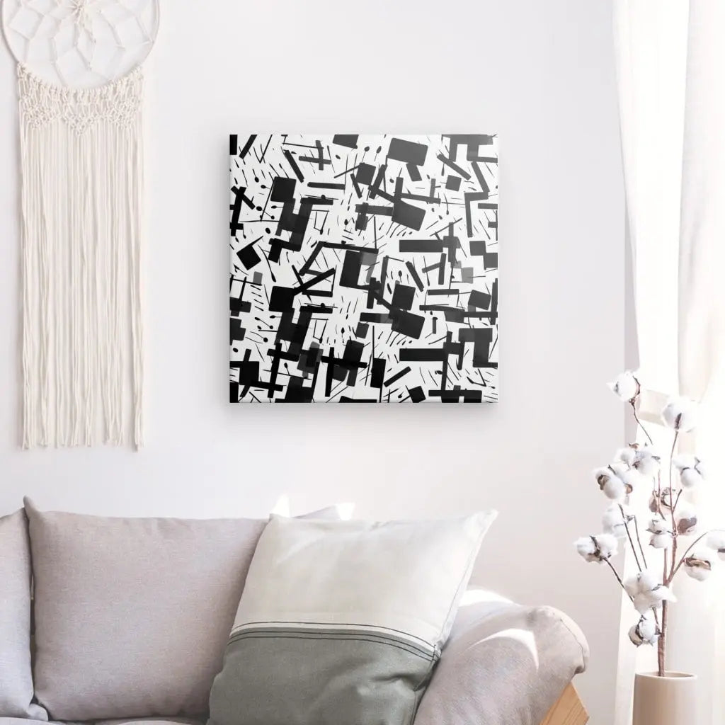 Un Tableau Art Abstrait Confettis Noir et Blanc avec des formes géométriques en noir et blanc est suspendu sur un mur blanc au-dessus d'un canapé gris clair décoré d'oreillers. Une tenture murale en coton et macramé rehausse la décoration moderne, créant une ambiance cohérente et élégante.