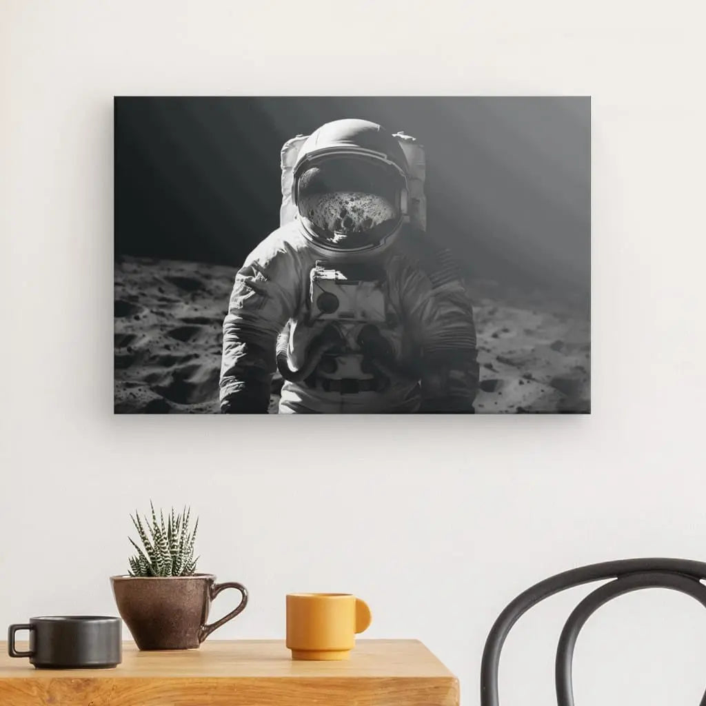 Un Tableau Portrait Astronaute Lune Voyage Interstellaire Noir et Blanc est exposé sur un mur au-dessus d'une petite table avec une plante en pot et deux tasses. Une partie d'une chaise est visible à droite.