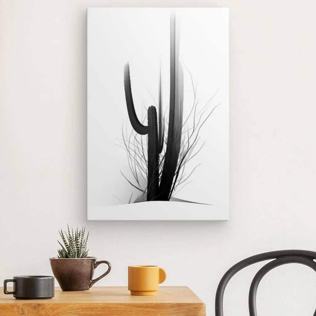 Un Tableau Cactus Minimaliste Art Moderne Abstrait Noir et Blanc est accroché à un mur clair au-dessus d'une table en bois avec une petite plante en pot, une tasse grise et une tasse jaune. La pièce Noir et Blanc Art Moderne Abstrait ajoute de l'élégance au décor, tandis qu'une chaise en métal noir est partiellement visible à droite.