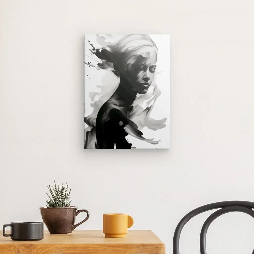 Un portrait monochrome d'une femme avec des éléments abstraits, intitulé "Tableau Femme Peinture Energique Eclaboussures Noir et Blanc", est accroché sur un mur blanc au-dessus d'une table en bois avec une petite plante en pot et deux tasses. Une chaise noire est partiellement visible à droite, complétant ce tableau noir et blanc de l'art contemporain.