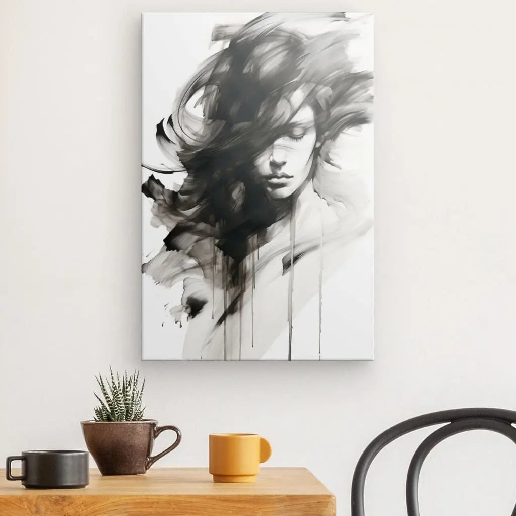 Un Tableau Portrait Féminin Aquarelle Noir et Blanc en noir et blanc représentant une femme sur toile, avec des coups de pinceau dynamiques, est accroché sur un mur blanc au-dessus d'une table en bois avec une petite plante, une tasse marron et une tasse jaune. Cette œuvre d'art captivante ajoute de l'élégance à l'espace.