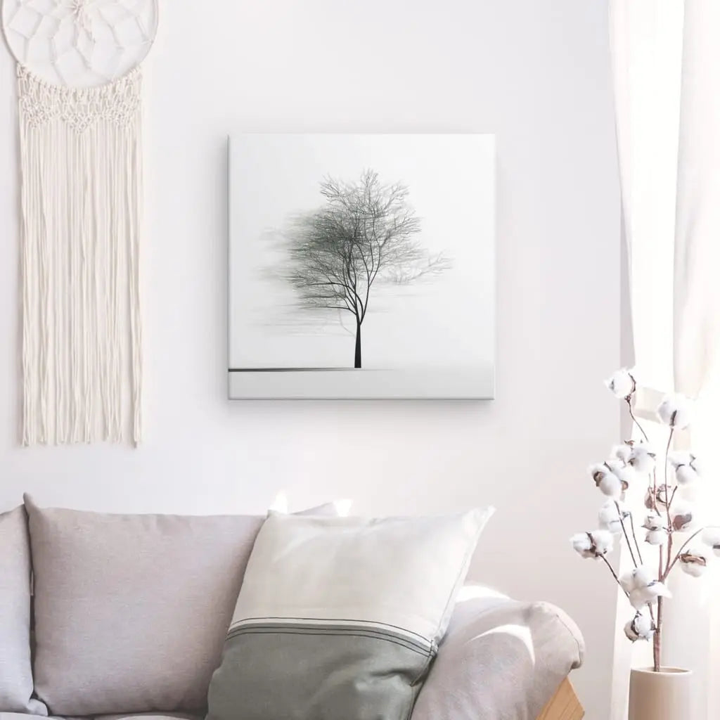 Salon minimaliste avec un canapé gris, un oreiller blanc, une branche de coton dans un vase, un macramé mural et un tableau Arbre Minimaliste Nature Originale Noir et Blanc encadré au mur. Les rideaux blancs laissent entrer la lumière naturelle.