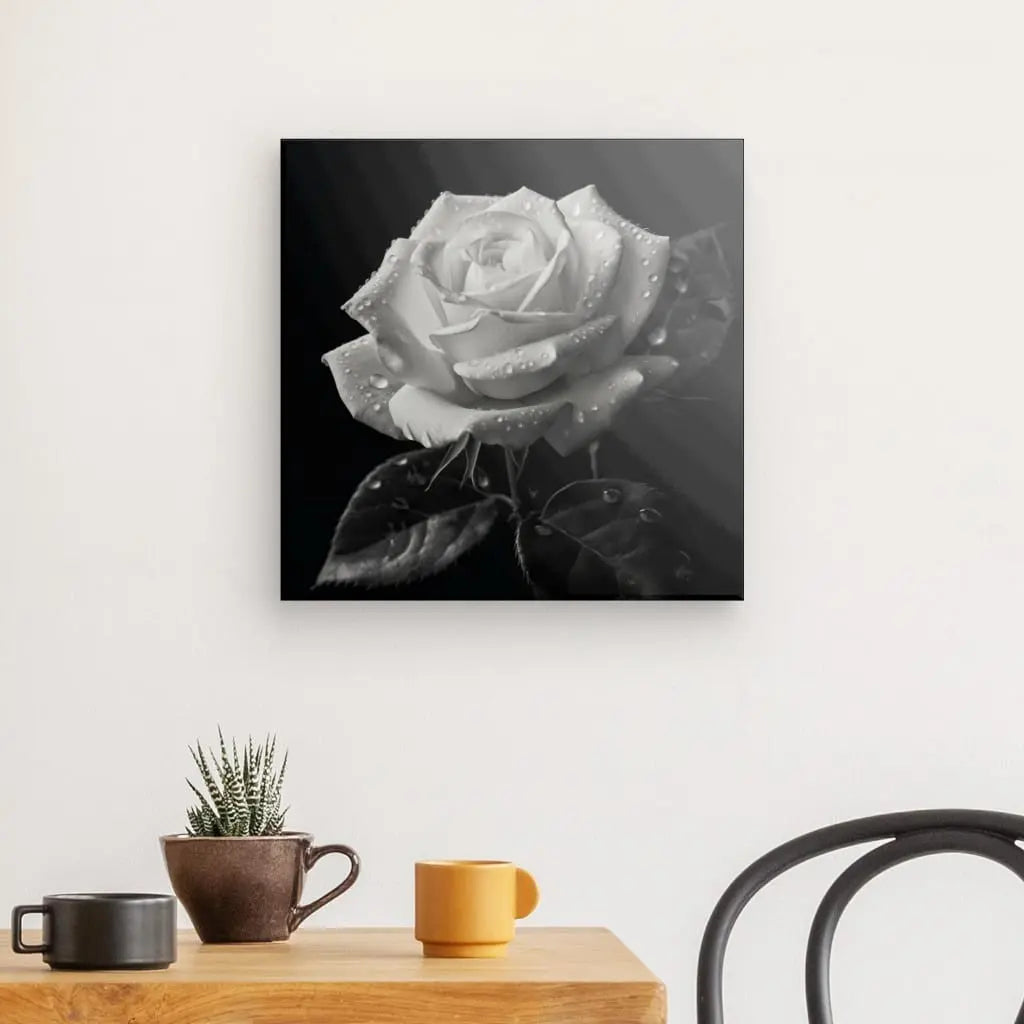 Tableau Rose Nature Morte Fleur Noir et Blanc représentant une rose avec des gouttelettes d'eau, exposée comme art mural au-dessus d'une table avec une plante et une tasse.