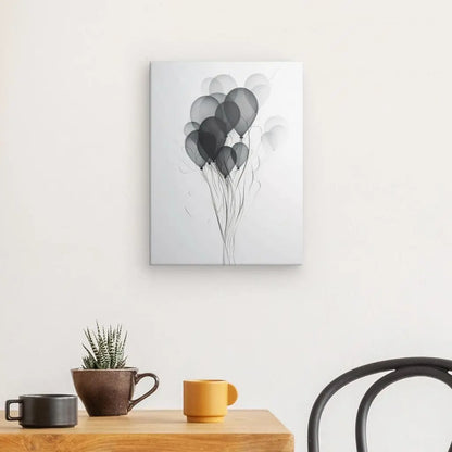 Un Tableau Ballons Baudruche Abstrait Design Noir et Blanc représentant des ballons en niveaux de gris est suspendu à un mur au-dessus d'une table en bois avec une plante en pot et une tasse jaune.