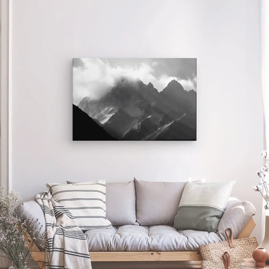 Un Tableau Montagnes Rocheuses Paysage Alpes Noir et Blanc, réalisé avec des encres latex HP sur toile, est suspendu au-dessus d'un canapé confortable avec des coussins dans un salon bien éclairé.