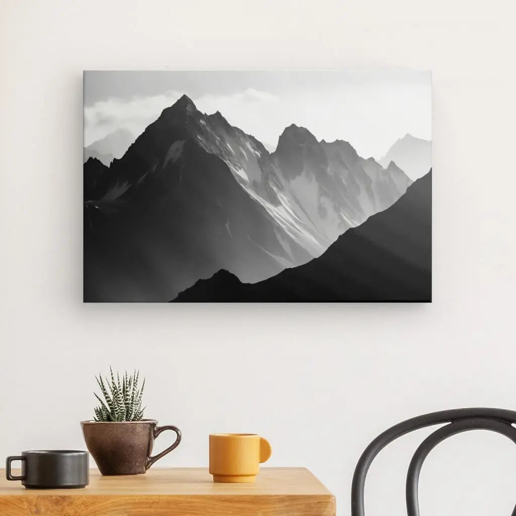 Tableau Monochrome Photo Pyrénées Montagnes Toile monochromes sur un mur au-dessus d'une simple table avec une plante et une tasse.